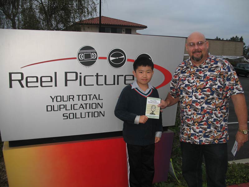 Perry Chen and Keith Wright standing in front of a large sign with the Reel Picture logo